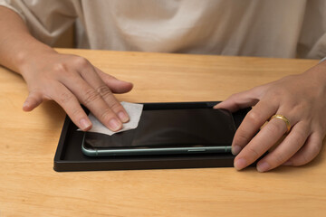 Hands cleaning smartphone screen with wipe before installing screen protector on wooden desk surface