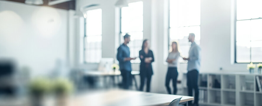 Four people stand talking near a window in a bright office space.