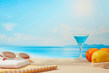A relaxing beach setup with sunglasses, citrus fruits, and a blue cocktail resting on a striped...