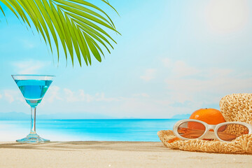 A tropical holiday scene with a woven hat, oranges, and a blue cocktail under the shade of palm leaves, with the endless sea and soft sunlight in the background.