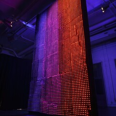 Large illuminated wall of square light panels, displaying gradient of pink and orange hues