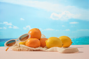 Oranges and lemons with sunglasses lie on a soft pastel surface. The turquoise pool and bright sky in the background highlight the freshness of summer wellness.