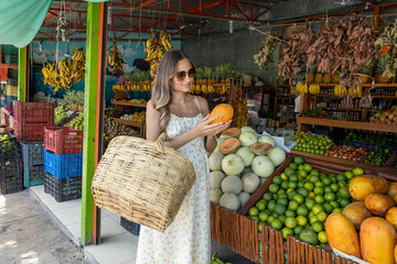 Pregnant woman weared in a light floral dress is shopping for fresh organic tropical fruits at a...