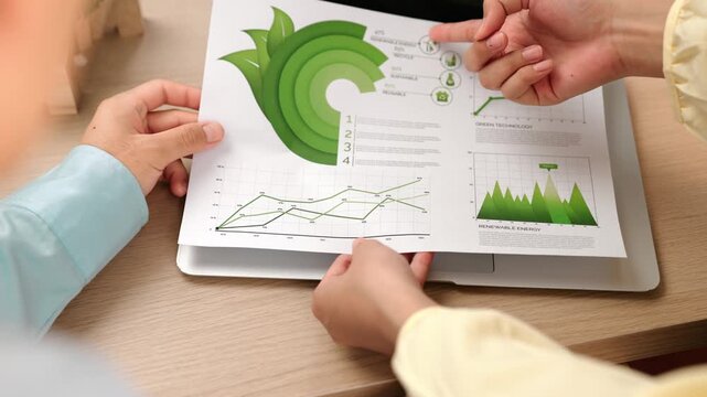 Businesswoman holding green energy graph present using clean energy for esg, environment, social and governance or decreasing carbon footprint to businessman working on laptop at company. Delineation.