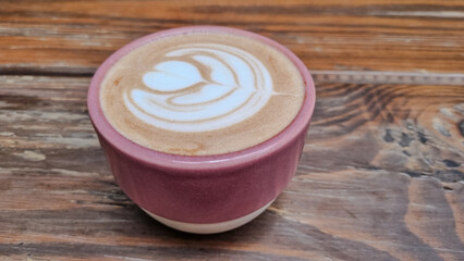 Delicious hot chocolate served in a pink ceramic cup with delicate latte art, set on a rustic wooden table. Cozy cafe atmosphere with a touch of handmade charm
