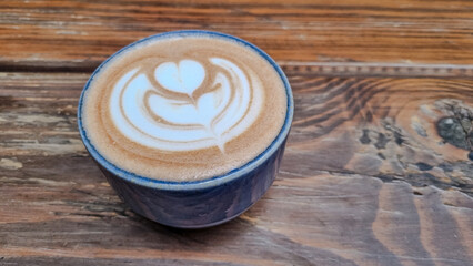 Ceramic cup filled with hot chocolate featuring elegant latte art on top, placed on a rustic wooden table. Cozy and warm atmosphere perfect for breakfast or coffee break