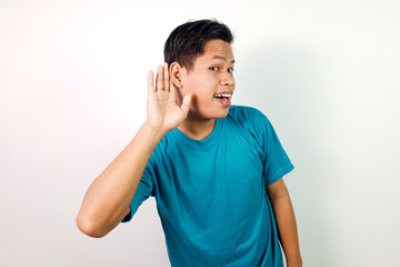 A smiling young Asian man wearing a blue shirt gestures with his hand to indicate listening, set...