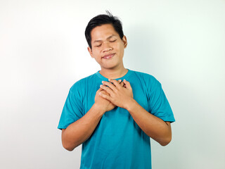 Portrait of a young Asian man expressing gratitude with a happy smile, hands crossed on his chest,...