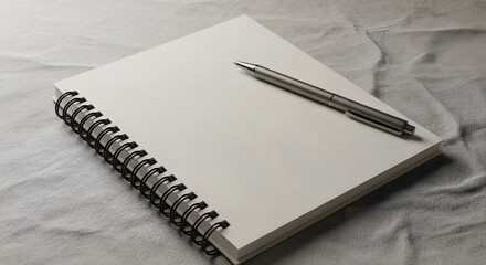 A spiral notebook with blank pages and a silver pen resting atop a textured surface. The image exhibits neutral tones and detailed textures.