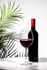 glass of non-alcoholic red wine is displayed alongside a bottle, complemented by palm leaves and a...