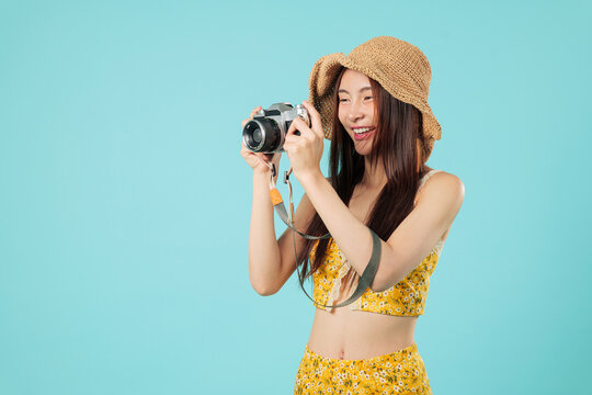 Happy young Asian woman tourist holding camera reviewing the photo on screen, for her travel memories she smiles as she gets ready to travel again, headshots isolated studio blue background