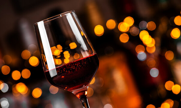 glass of red wine stands elegantly against a backdrop of warm, blurred lights, creating a cozy atmosphere for an evening gathering.