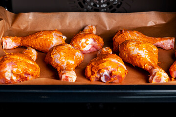 Raw chicken drumsticks in smoked paprika, spices, oil marinade, on a baking sheet in the oven, top view
