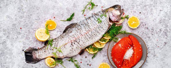 Gutted and cleaned raw trout and fresh red caviar with lemon, dill, salt and spices on gray table background, top view