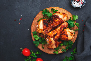 Baked chicken legs or drumsticks in hot chili paprika pepper marinade on wooden serving board, black background, top view
