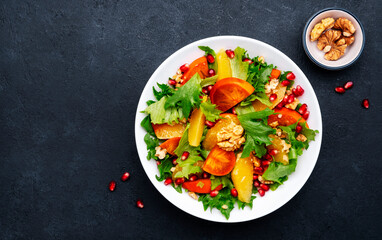 Delicious vegan salad with fresh persimmon, pomegranate seeds, walnuts, orange slices and lettuce