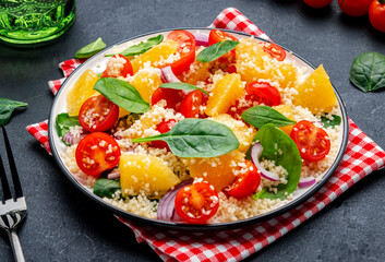 Gourmet vegan salad with couscous, tomatoes, onion, spinach and orange. Black background, top view