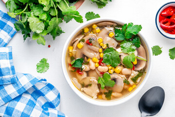 Mexican style chicken soup with mushrooms, corn, white beans, hot chili and cilantro. Black table background, top view