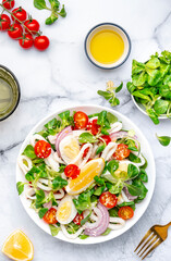 Seafood salad with squid, orange, tomatoes, lamb lettuce and olive oil with lemon juice dressing, gray table background, top view