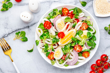 Seafood salad with squid, orange, tomatoes, lamb lettuce and olive oil with lemon juice dressing, gray table background, top view