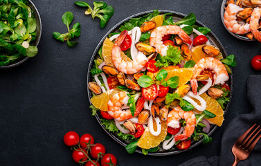 Delicious seafood salad with shrimp, mussels, squid, oranges, lettuce and olive oil with lemon dressing, black background, top view