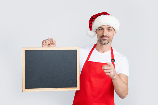 cheerful mature man in santa hat and apron hold blackboard with copy space. point finger - Powered by Adobe