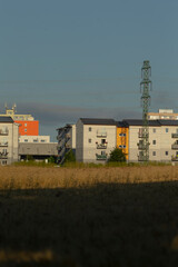 In the foreground, a wide and open field stretches out, leading to a row of modern apartment...