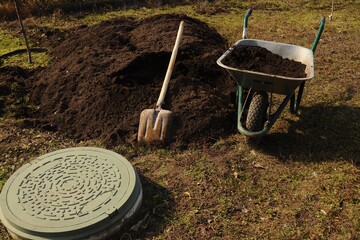 A sunny outdoor scene with a wheelbarrow, soil, and gardening tools.