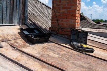 Tools sit on a rusty rooftop, suggesting repair work under a bright blue sky.