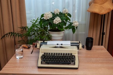 A vintage typewriter with a blank paper sheet, surrounded by plants and accessories.
