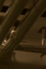 A large assortment of pipes is suspended from the ceiling in a dimly lit room, creating an...