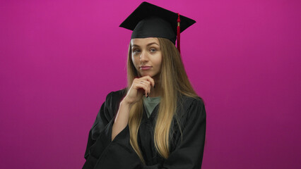 Woman in graduation cap and gown thinking against pink background isolated