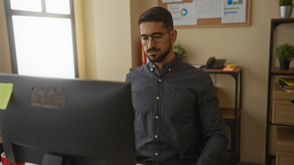 Young man stretching neck in an office setting with a computer, showcasing a relaxed, professional...