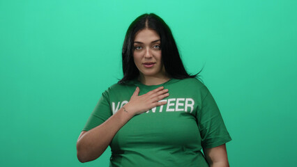Curvy woman volunteer in green shirt stands over isolated green background wall, embodying...