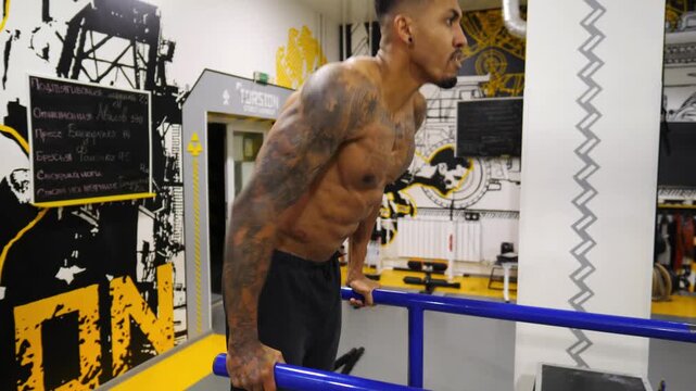 Strong man doing push ups on parallel bars at sport club. Muscular sportsman with tattoos doing hard exercises modern gym. Concept of healthy and active lifestyle. Slow motion
