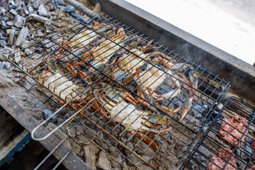 Raw blue crabs grilling over charcoal at a seaside barbecue