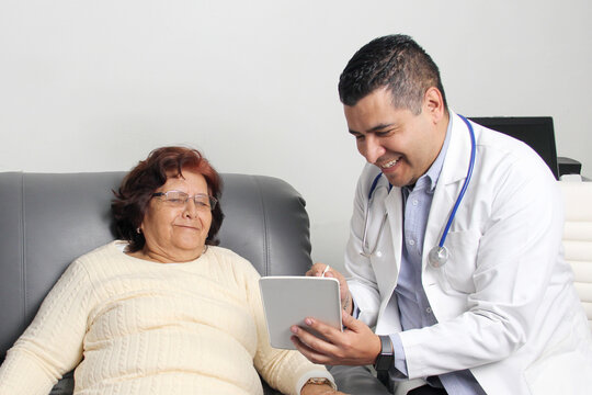 An elderly Latina woman in consultation with a geriatric specialist for a checkup notes her symptoms with the office