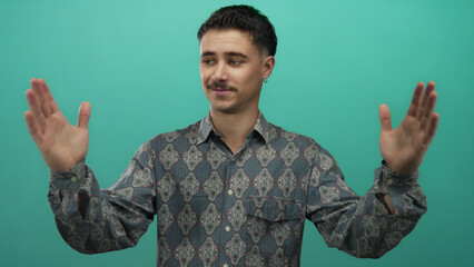 Young hispanic man making large gesture with hands in front of isolated green background wall,...