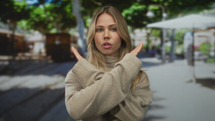 Fototapeta premium Blonde woman wearing beige turtleneck sweater crossing hands in x gesture on street; denial rejection.