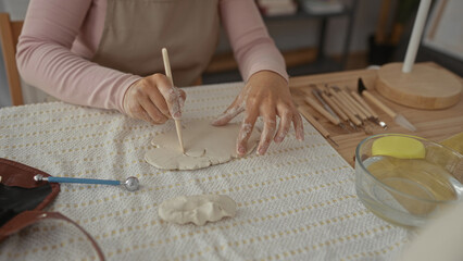 Woman uses bare hands and wooden tool to carve clay slab in pottery studio; creativity focus...