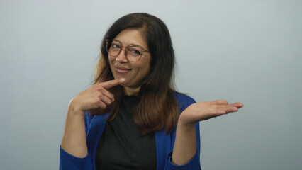 Woman wearing blue jacket smiling and finger pointing to open palm in studio with light blue...