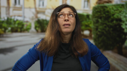 Fototapeta premium Middle-aged hispanic woman holds forehead in pain on sunny urban street; discomfort stress fatigue headache.