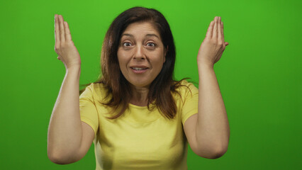 Middle aged hispanic woman wearing yellow shirt covers eyes with both hands in studio;...