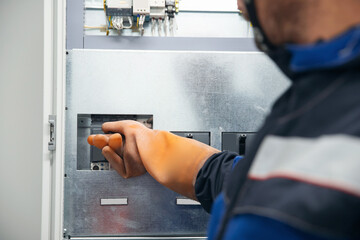 Electrician worker turns on equipment in switchboard of power plant, his hand wearing an...