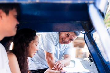 Middle-aged Southeast Asian driver smiles as he returns change to a young female passenger, both...