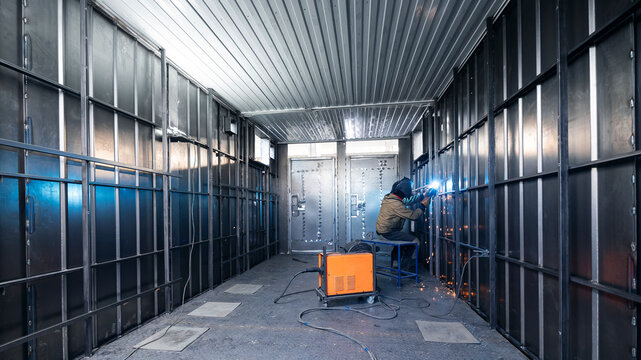 Caucasian male welding in industrial factory room with metal walls and equipment