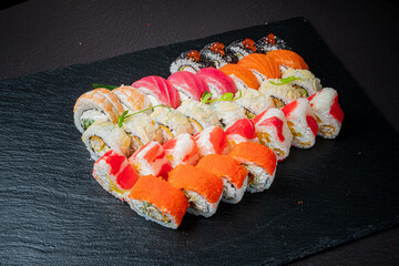 A colorful array of sushi rolls presented on a dark slate board, showcasing fresh seafood