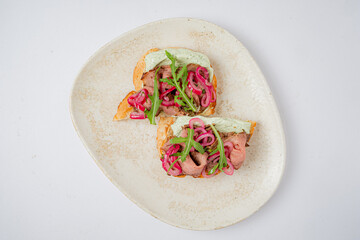Colorful open-faced sandwich showcases tender meats topped with pickled onions and fresh greens