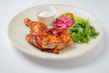 Juicy grilled chicken leg served on a plate with fresh greens, tangy pickles, and a rich sauce