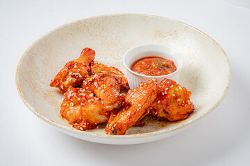 Crispy chicken wings coated in spicy glaze and sesame seeds alongside a tangy dipping sauce